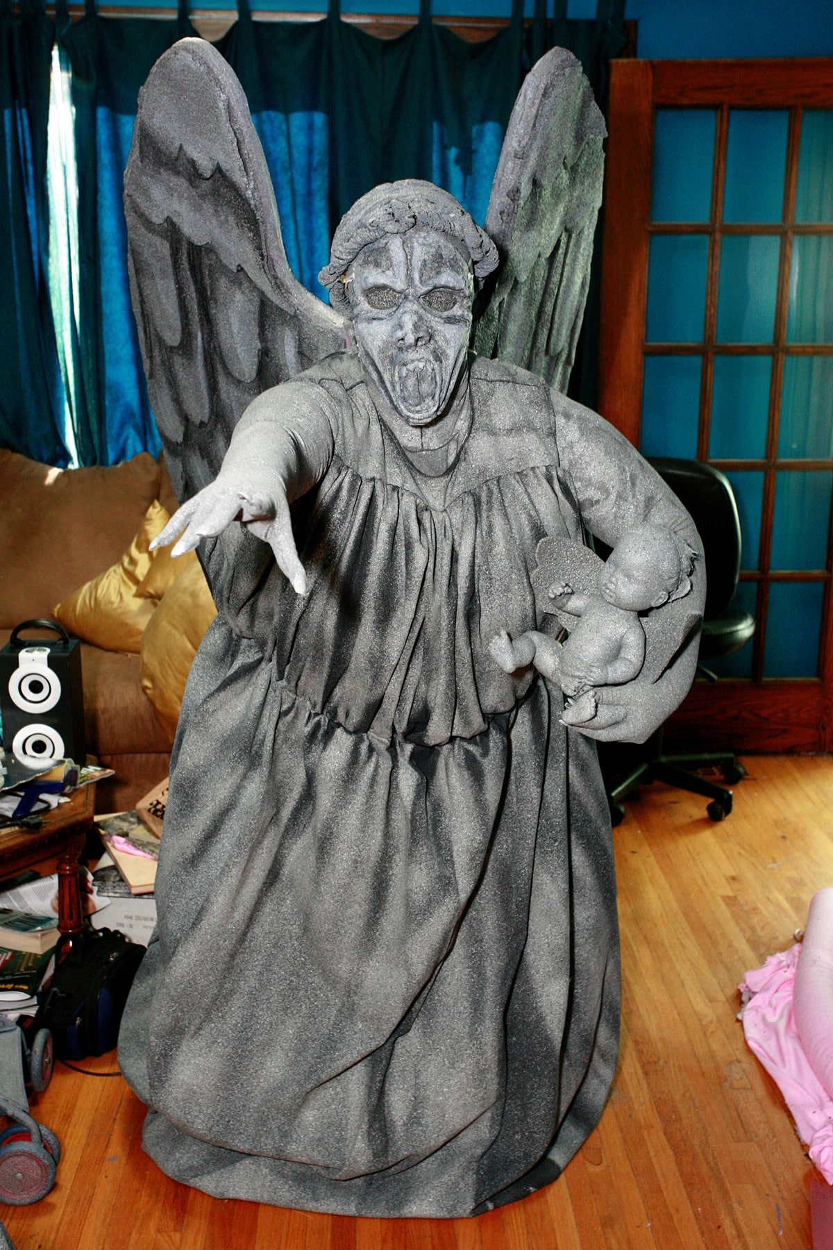 A person dressed as a weeping angel statue, holding a baby weeping angel doll.