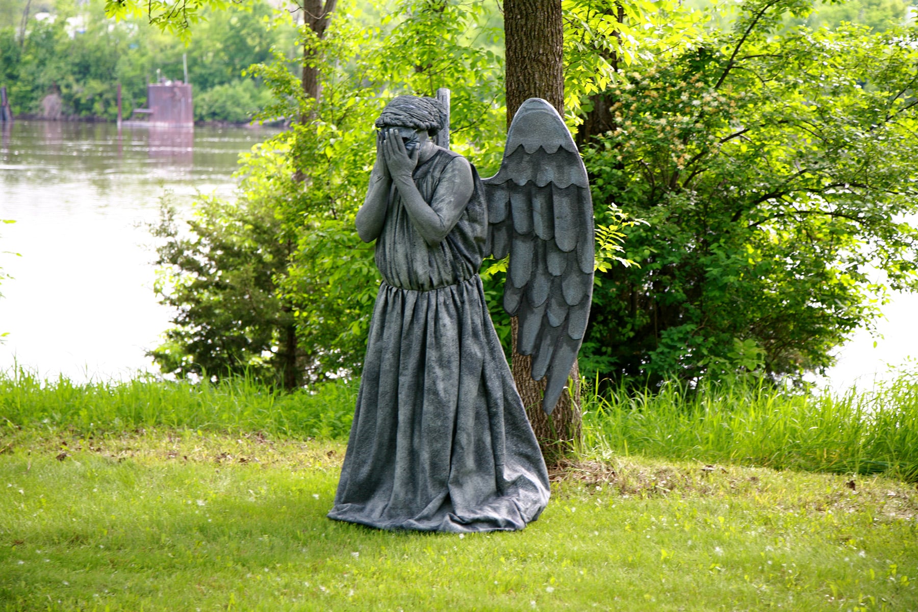 A person dressed as a weeping angel statue in a park.