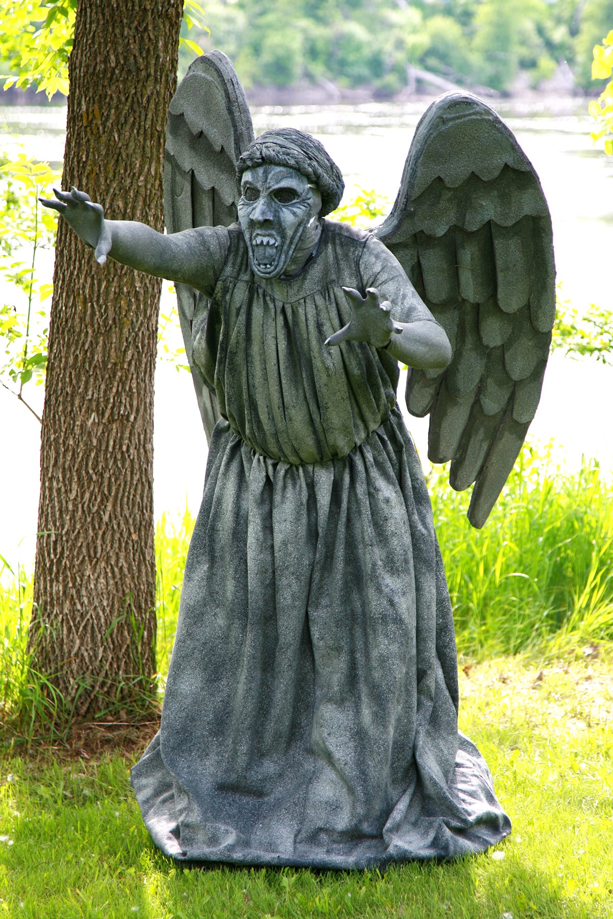 A person dressed as a weeping angel statue in a park.