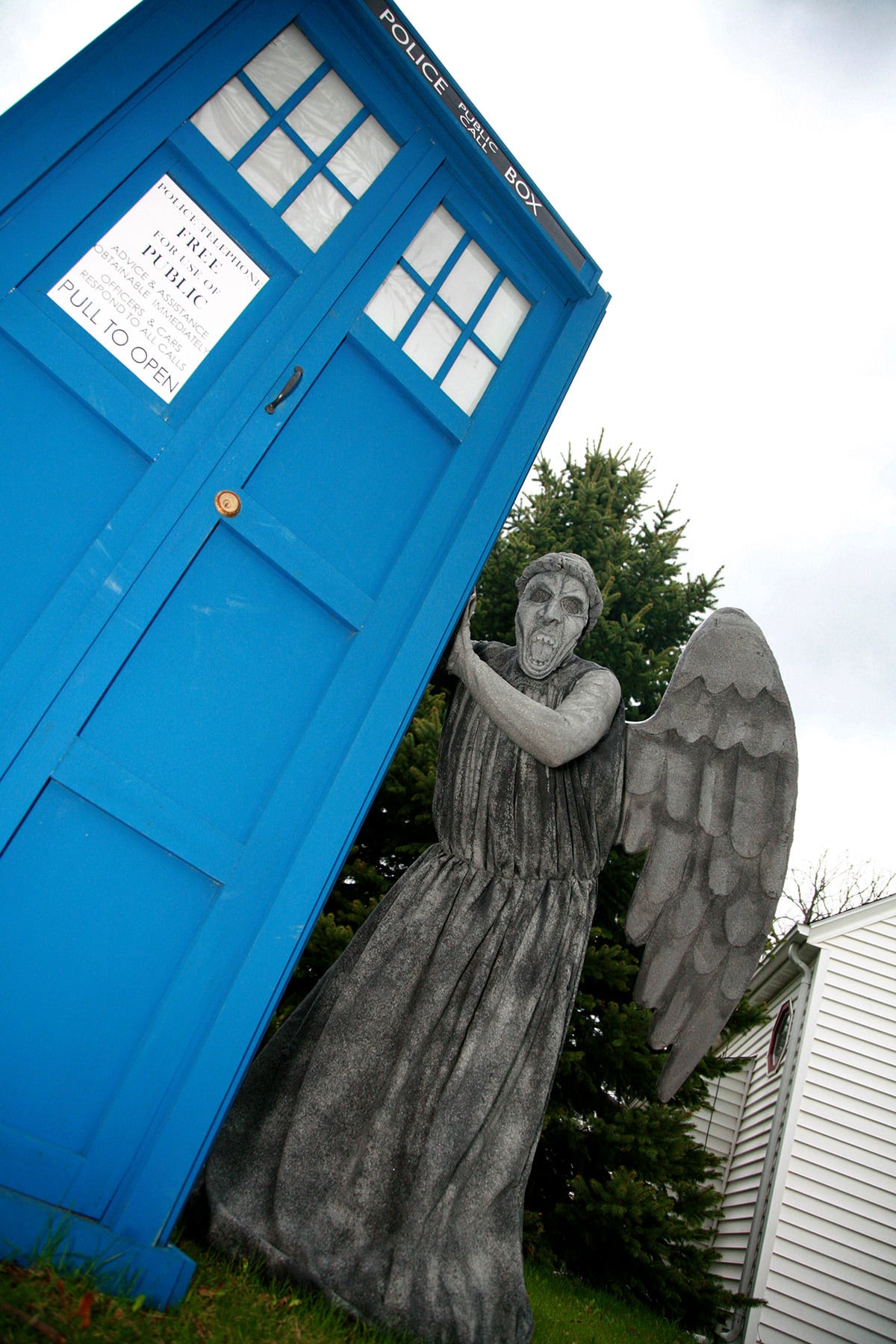 A person dressed as a weeping angel, leaning on a full sized TARDIS.