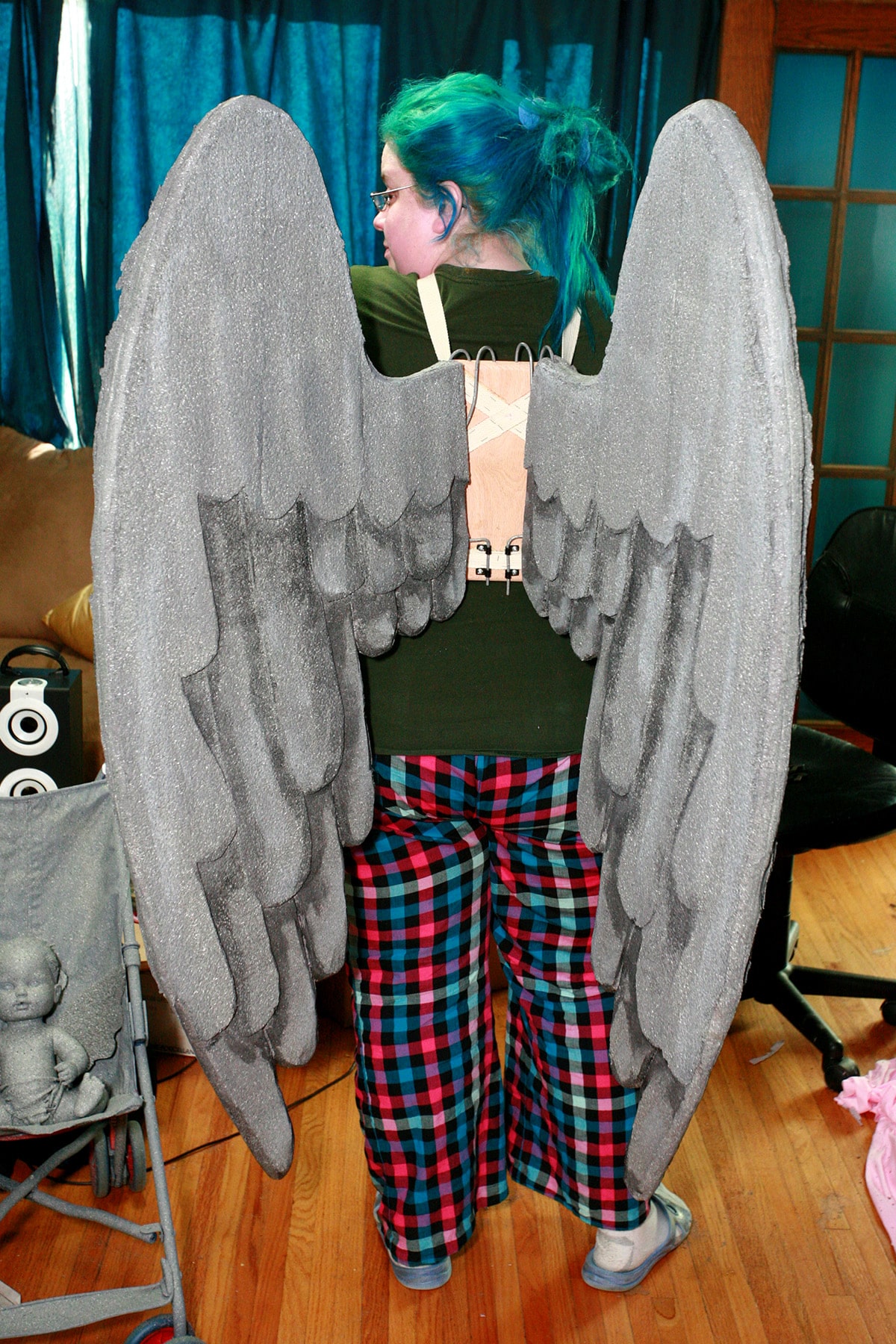 A woman in bright PJ pants has a harness and set of large grey angel wings on her back.