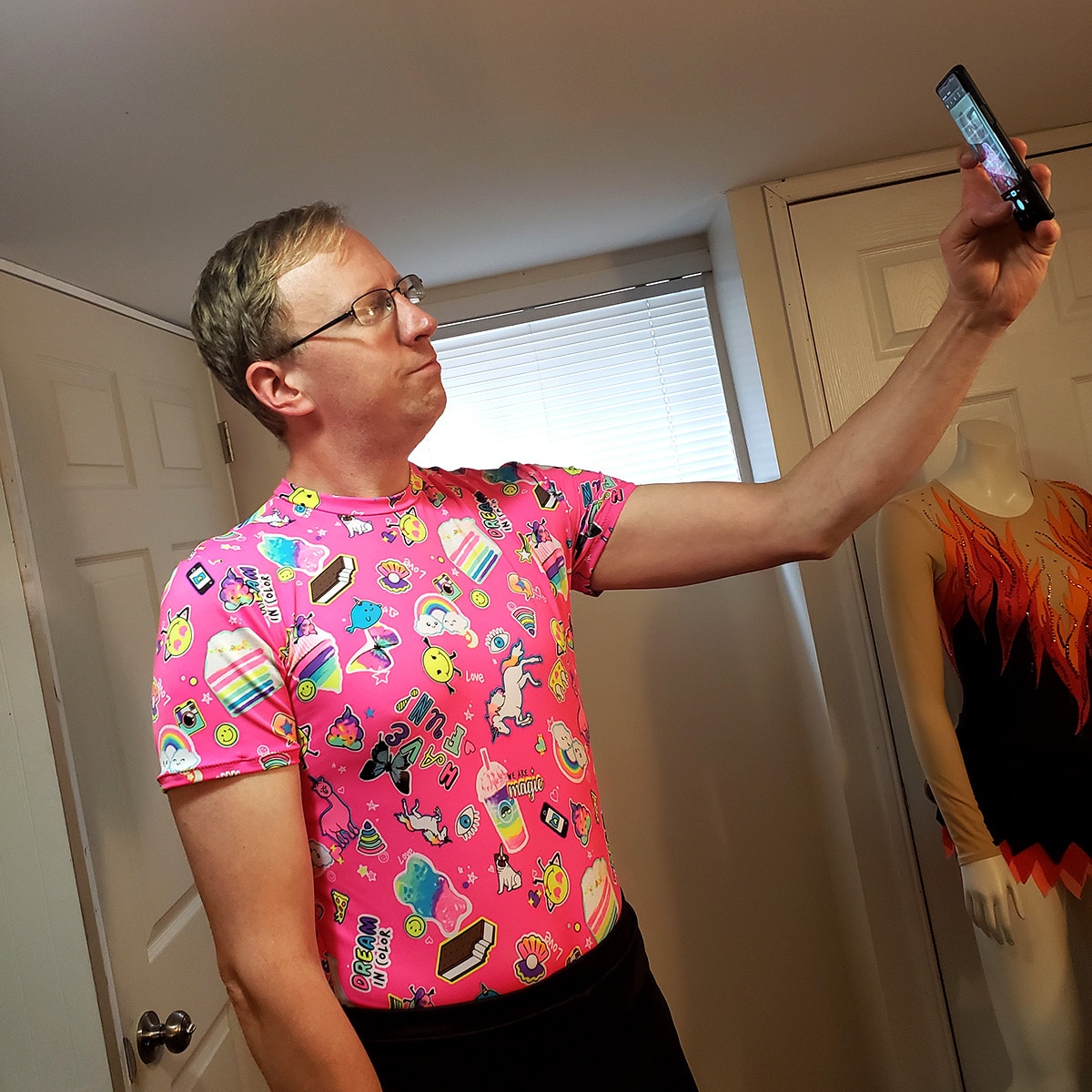 A middle aged man in a bright pink patterned figure skating costume takes a selfie.
