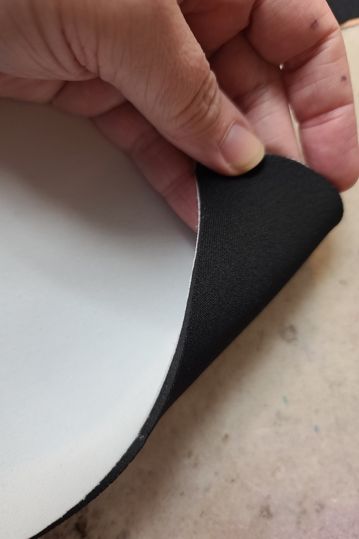 A hand lifts the corner of a piece of white bra padding, showing the underside is black.