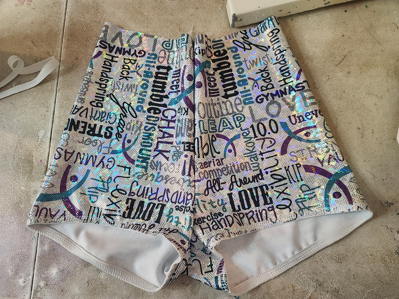 White, purple, and black holo print booty shorts with elastic sewn into the leg openings.