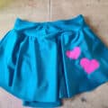 An unhemmed turquoise figure skating skirt with pink hearts on one hip.