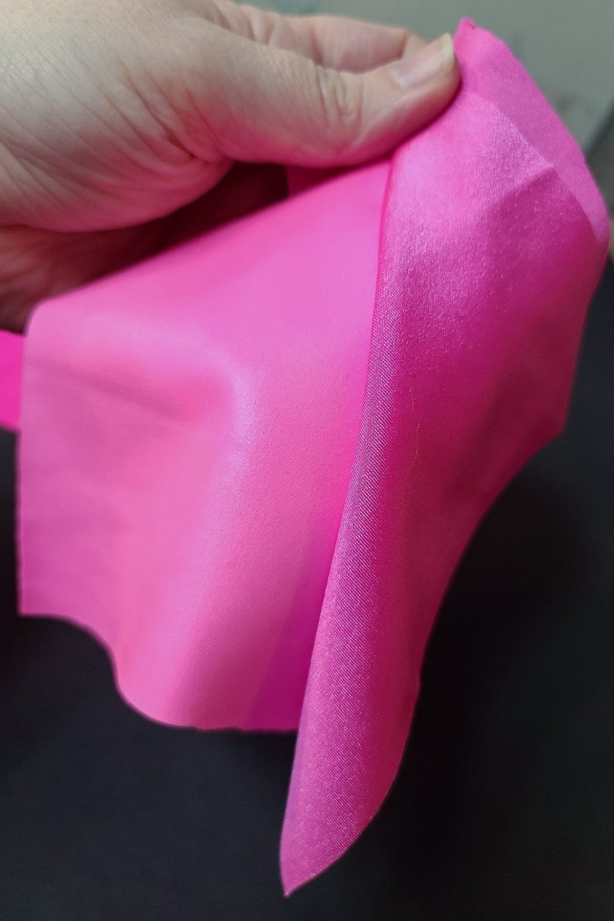 A hand holding a piece of shiny pink spandex next to a piece of wet look pink spandex.
