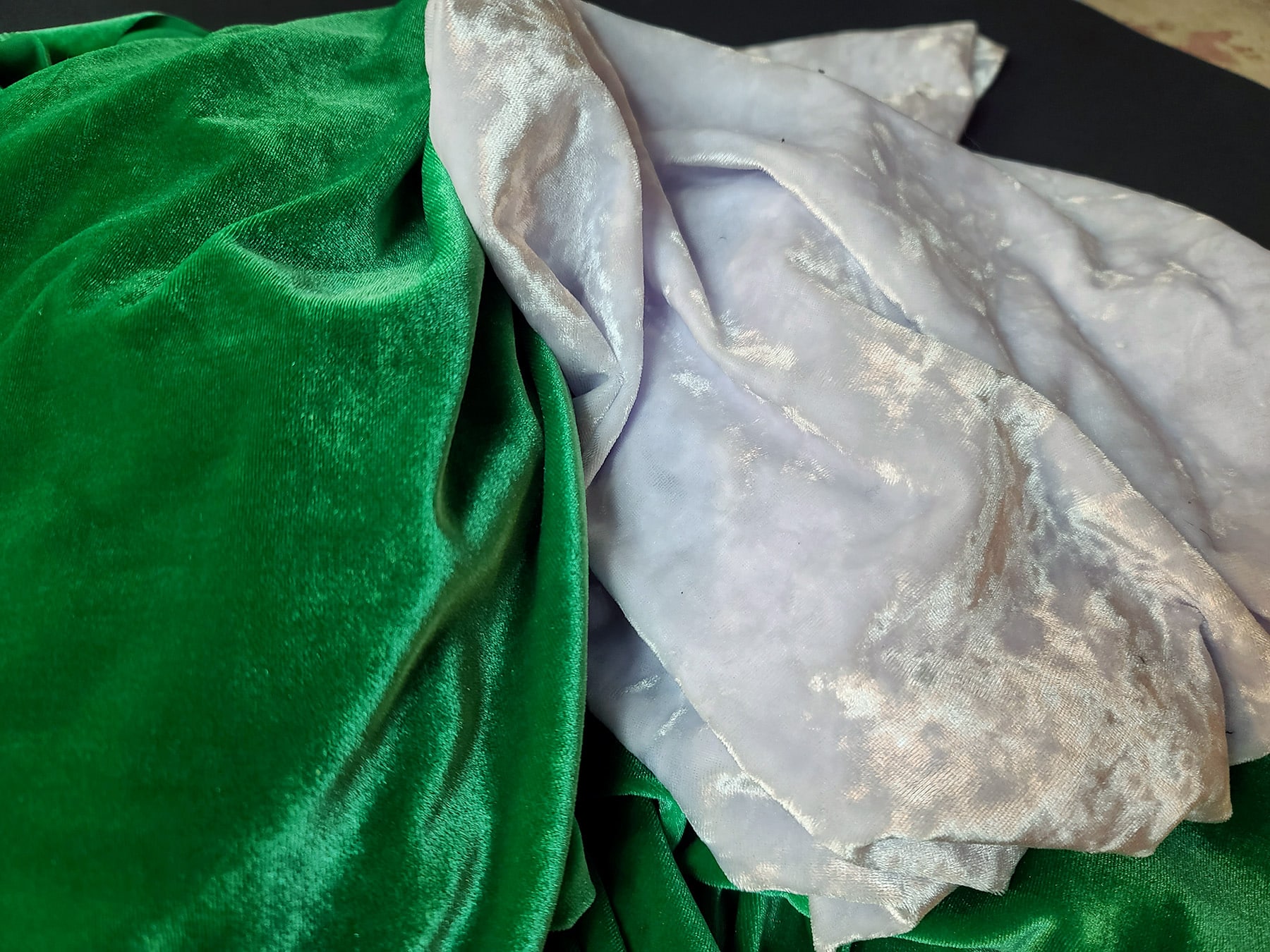A piece of green spandex backed velvet next to a piece of white crushed spandex velvet.