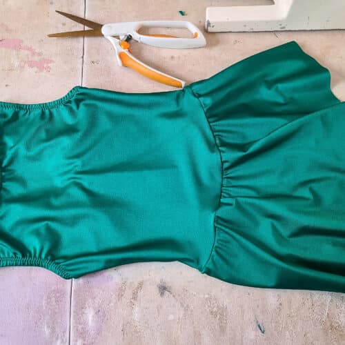 A basic green figure skating dress laying on a sewing table.