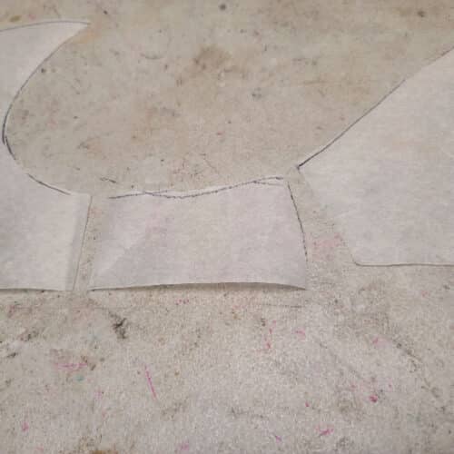 The lower part of the front crotch of the pattern piece cut off, laying next to the rest of the pattern piece.