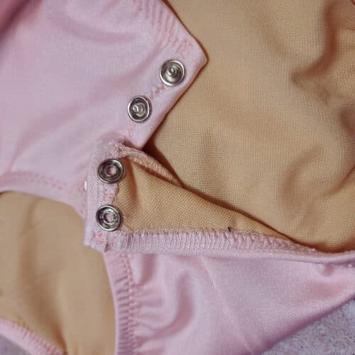 The bottom of a pink bodysuit, showing off the hollow metal snaps used to close it.