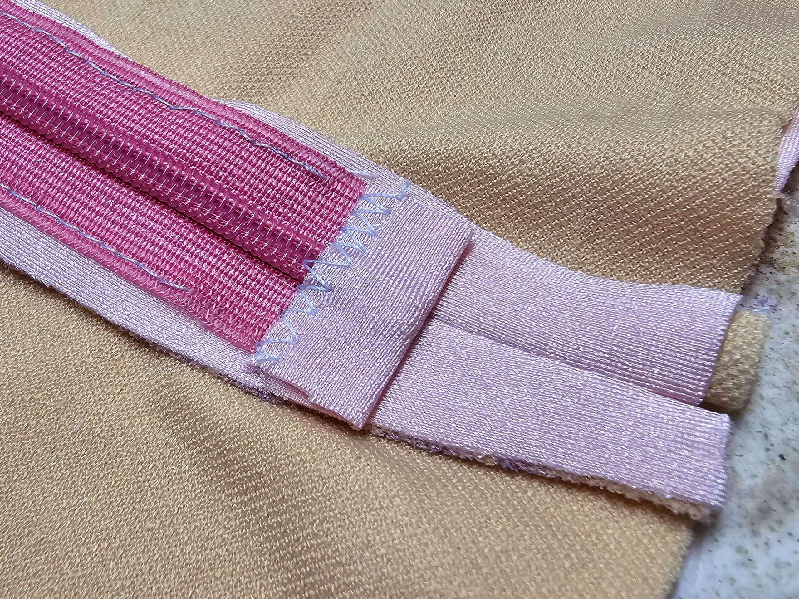 The bottom edge of an invisible zipper, with pale pink spandex binding the bottom edge.