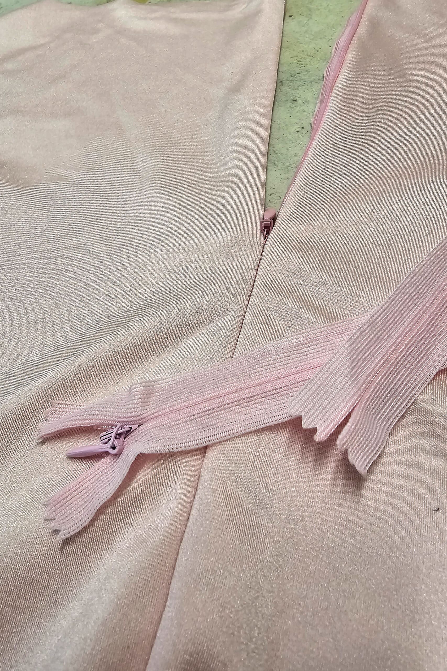 A pink bodysuit with a partially unzipped invisible zipper, and 2 more invisible zippers laying across it.