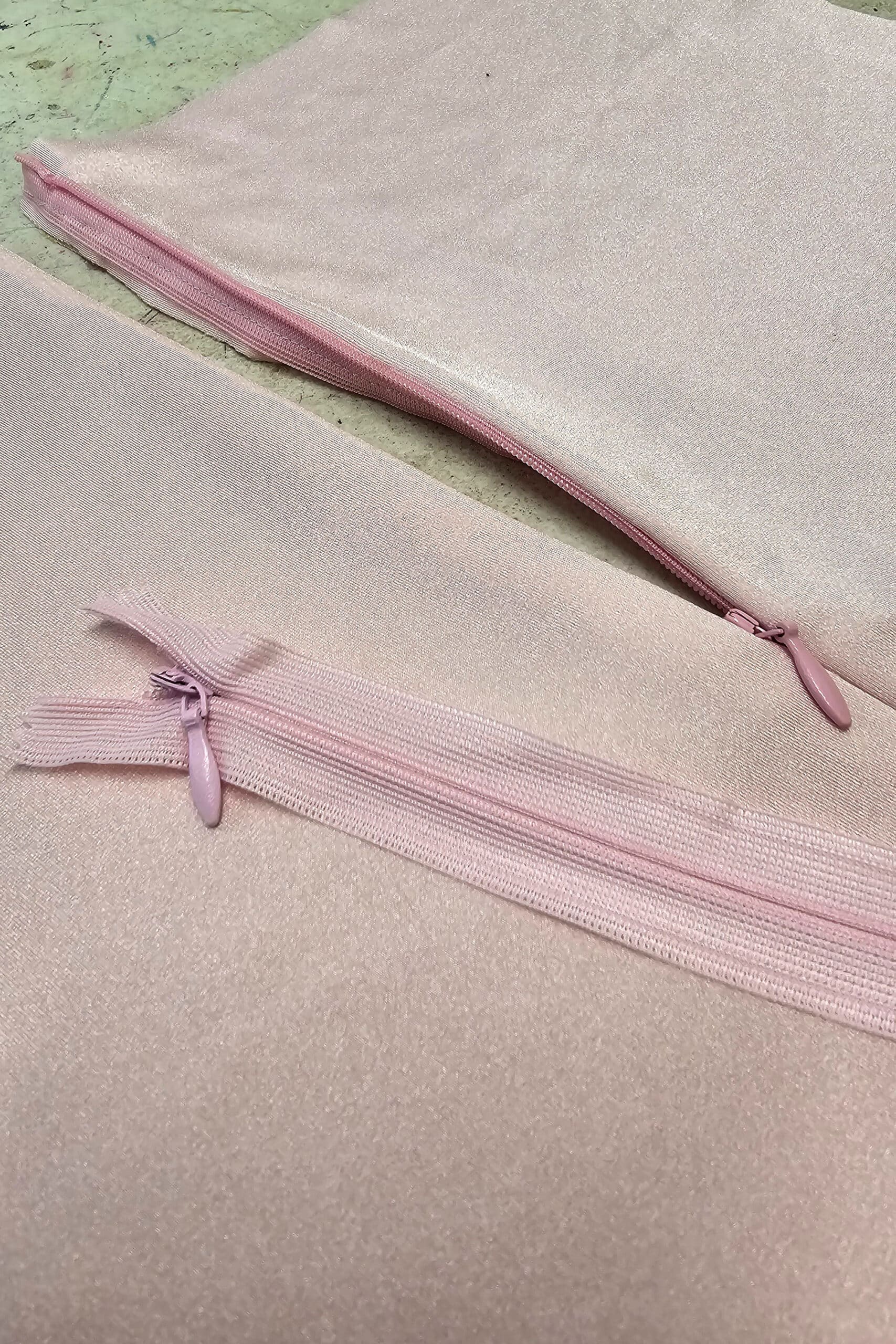 A pink bodysuit with a partially unzipped invisible zipper, and another invisible zipper laying across it.