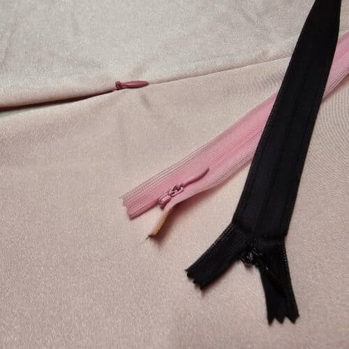 A pink bodysuit with a partially unzipped invisible zipper, and 2 more invisible zippers laying across it.