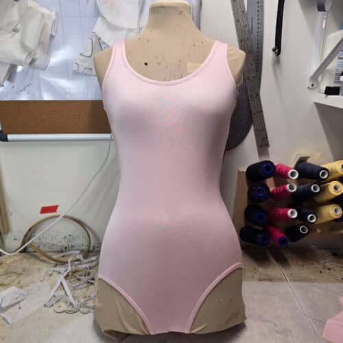 A basic bodysuit - pink - on a dressform. The dressform is on a sewing table.