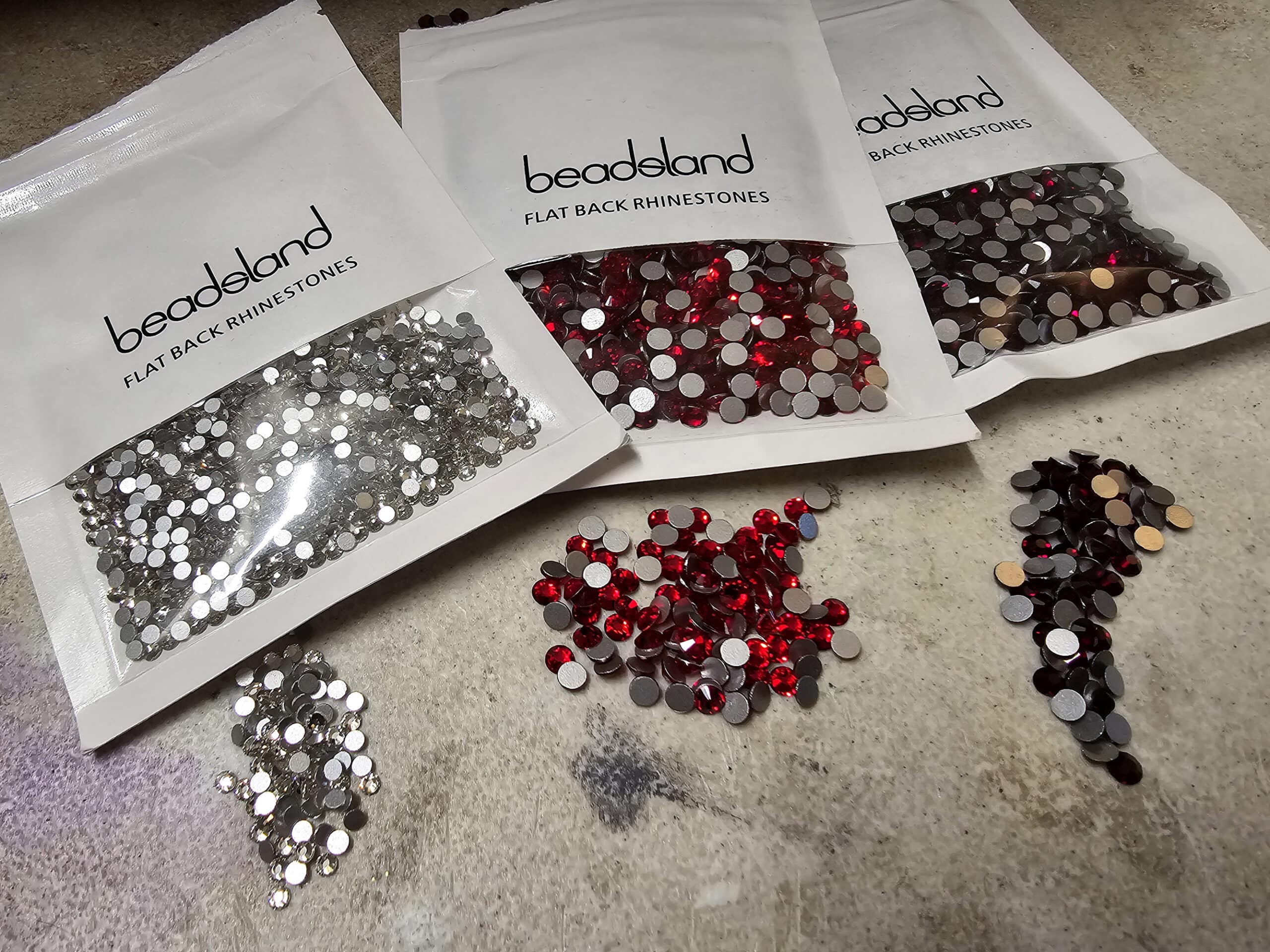 3 baggies of rhinestones, with clear, red, and dark red rhinestones in front of them.